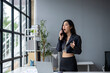 © apichat - A woman is talking on her cell phone in a room with a desk and a potted plant