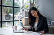 © apichat - A woman is sitting at a desk with a laptop and a cell phone