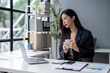 © apichat - A woman in a black jacket is sitting at a desk with a laptop and a cup of coffee