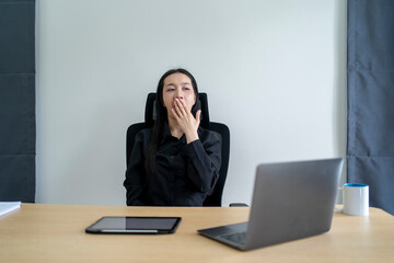 Tired asian businesswoman yawning while working on laptop in office