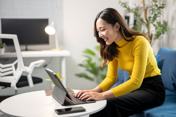 Wall Mural - young asian woman working from home using tablet and smiling