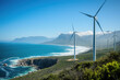 © Татьяна Евдокимова - Wind turbines generating clean energy on a green coastline with mountains in the background