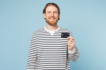 Wall Mural - Young smiling fun happy man he wear striped sweatshirt casual clothes hold in hand mock up of credit bank card isolated on plain pastel light blue cyan background studio portrait. Lifestyle concept.