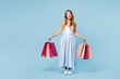 © ViDi Studio - Full body young smiling happy satisfied fun woman wear casual clothes hold in hand paper package bags after shopping look camera isolated on plain blue background. Black Friday sale buy day concept.
