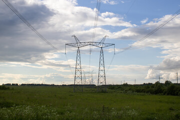 High voltage pylons against the blue sky with white clouds and bright green meadow. Power lines stretching into the distance. Perspective. Electricity