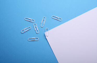 Wall Mural - White sheet of paper with paper clips on blue background