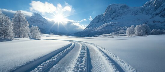 Wall Mural - A winding road through a snowy valley with towering mountains in the background and a bright sun shining in a clear blue sky.