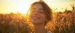 © GoDress - A young woman with closed eyes stands in a field of tall grass, bathed in the warm glow of the setting sun. Her smile radiates joy and peace.