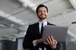 © Andrii Zastrozhnov - A man in a suit holding a laptop with a smile on his face. Concept of professionalism and confidence