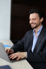 Wall Mural - A man in a suit is sitting at a table with a laptop in front of him. He is smiling and he is enjoying himself