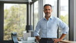 © MonteStudio - Middle-aged Hispanic businessman in a light blue shirt and dark trousers, leaning against desk in corporate office with large windows and natural light. Creative director. Planning, production stylist