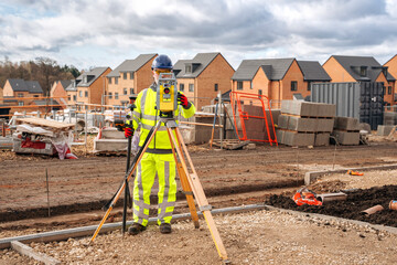 construction surveyor measuring land for new homes in an active development site under cloudy skies