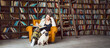 © Iryna&Maya - Weekend in library with interesting book. young woman covered in blanket sitting in orange chair with small dog pug in big library with many book shelves on the background. Long horizontal banner