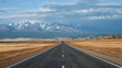 © dlogvin - Driving on highway of black asphalt and white road markings at sunny day, road going into distance through desert prairie at autumn to snowy mountain summits on horizon in wild. Pov from moving car