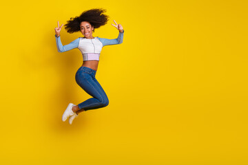 Wall Mural - Full body photo of attractive young woman jump show v-sign dressed stylish blue clothes isolated on yellow color background