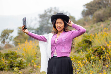 Foto de una feliz y bonita campesina con un sombrero hablando por un teléfono celular en los Andes peruanos. Mujer usando teléfono móvil