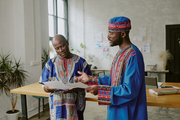 African American coworkers in traditional clothes discussing new startup while working offline in modern office