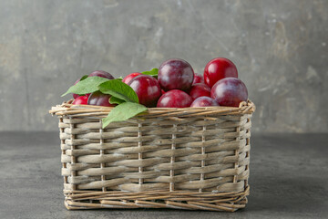 Canvas Print - Tasty ripe plums and leaves in wicker basket on grey textured table