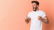 © Maksym - A man gritting his teeth, fists clenched at his sides, showing frustration and anger, standing against a light pastel peach background.