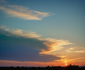 Leinwandbilder - A breathtaking sunset paints the sky with hues of orange, yellow, and blue, casting a warm glow over the silhouetted trees and rolling hills in the distance