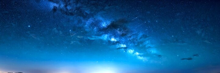 Leinwandbilder - A panoramic view of the night sky, featuring the Milky Way galaxy and a few shooting stars, with a dark blue hue and a faint outline hill in the bottom left corner