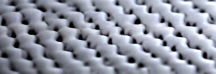 Fototapete - A close-up view textured surface, possibly a fabric or a material, with a repeating pattern of small, dark gray squares