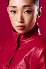 Wall Mural - Fashionable asian woman in red leather jacket posing confidently against a red background in a studio setting