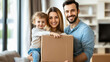 © Dina Photo Stories - Happy family relocation to new apartment. Smiling man and woman holding big cardboard box with their child inside. Unpacking cardboard boxes. New home, rental real estate moving into apartment
