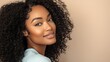 © atipong - Beautiful black woman with curly hair smiling in a light blue shirt exuding joy and warmth against a soft beige background perfect for lifestyle beauty and fashion themes.