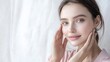 © atipong - Beautiful woman with clear skin and gentle smile hands touching her face hair pulled back wearing soft pink shirt highlighted features clean white background portrait photography.