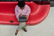 © Seventyfour - Top view of African American businesswoman typing on laptop keyboard while sitting comfortably on red designer furniture in modern office center, copy space