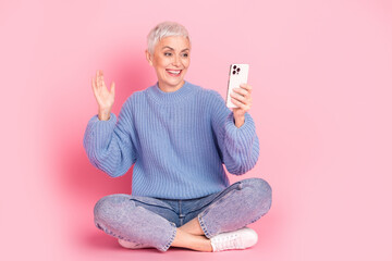 Sticker - Full size photo of attractive senior woman sit floor selfie photo wave hand dressed blue knitwear clothes isolated on pink background