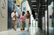 © Seventyfour - Wide angle shot of diverse group of three colleagues in smart casual clothing walking along business center hallway cheerfully talking after working day, copy space