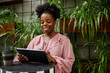 © Seventyfour - Medium shot of smiling businesswoman using digital tablet while working in cozy cafe at stand up desk next to green living wall with potted plants in modern office center, copy space