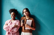 © Seventyfour - Portrait shot of two successful businesswomen from different ethnic backgrounds wearing elegant office clothing smiling at camera while standing against vibrant blue wall, copy space