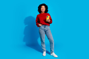 Full length photo of lovely young lady hold device dressed stylish red garment isolated on blue color background