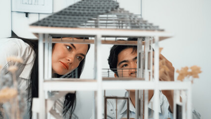 Close up of cooperative professional engineer working together to measuring house model structure. Young beautiful architect measure house model while male engineer support performance. Immaculate.