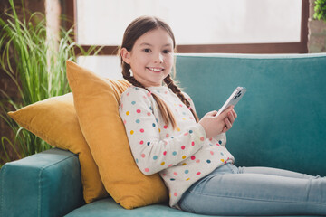 Poster - Portrait of charming little girl use smart phone sofa wear pullover modern interior flat indoors