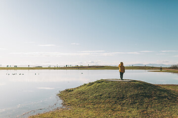 A little boy standing on top of a hill in front of a big pond. 