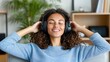 © Pinklife - A person in a light blue sweater with curly hair listens to music using large headphones while leaning back in a cozy indoor setting with a green plant in the background.
