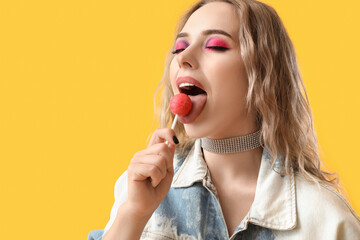 Poster - Young woman eating lollipop on yellow background, closeup