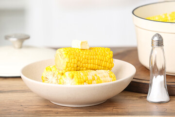 Bowl of boiled corn cobs with butter on wooden table in kitchen