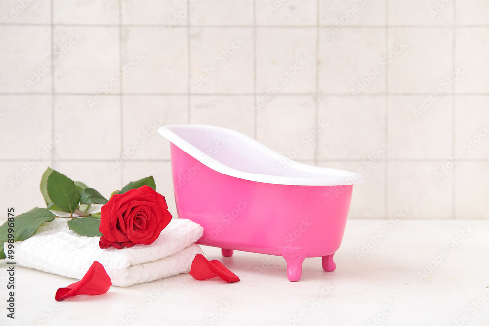 Small bathtub, rose flower and clean towel on light table