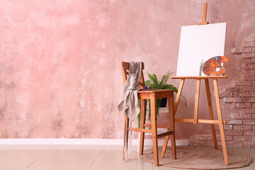 Sticker - Wooden easel with blank canvas and painting tools near color wall in artist's workshop