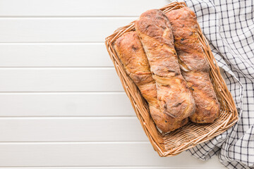 Canvas Print - Crusty rustic baguette in basket on white table. Top view.