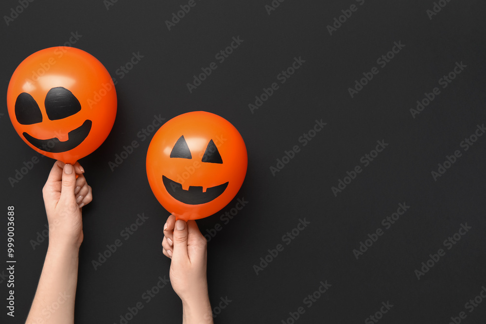 Female hands with funny Halloween orange balloons on black background