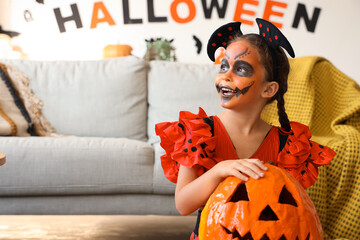 Wall Mural - Little girl dressed for Halloween as devil with pumpkin at home