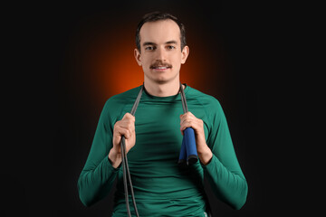 Young male trainer with skipping rope on dark orange background