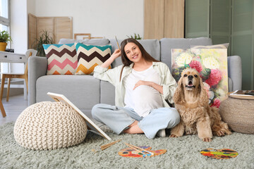 Canvas Print - Young pregnant woman painting while sitting on floor with dog and picture in room