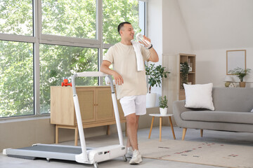 Canvas Print - Sporty young man drinking water near treadmill at home